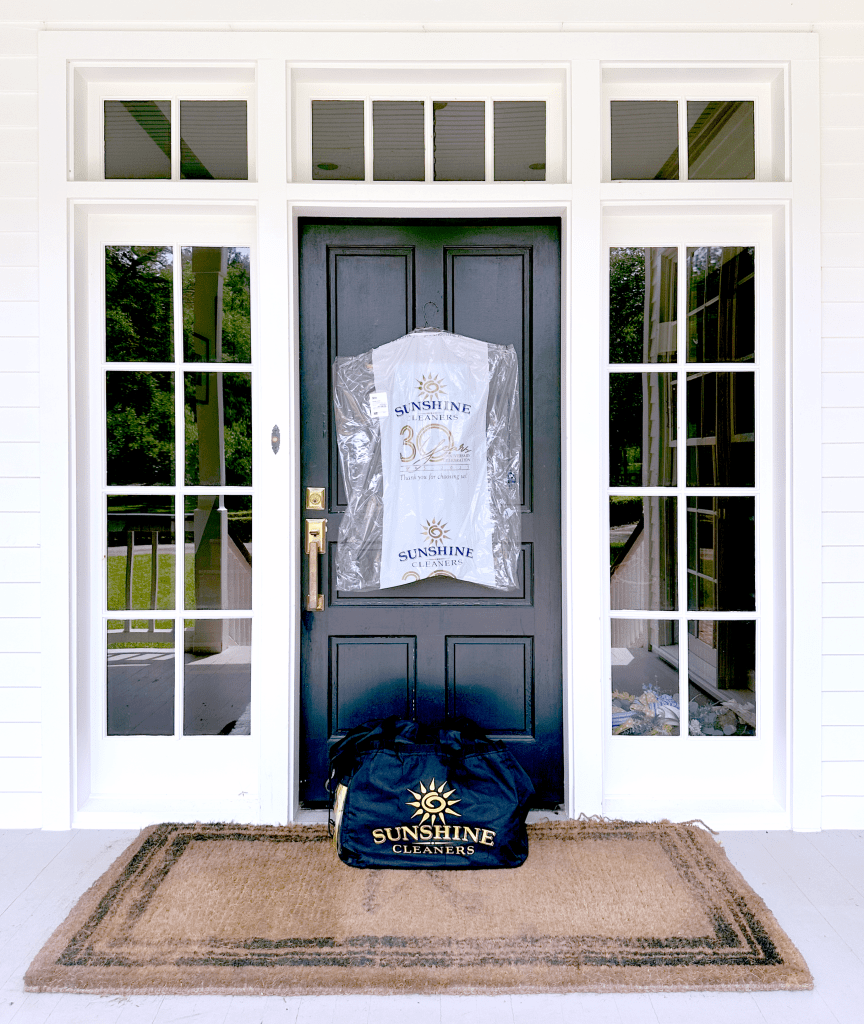 Front door with a black door and large windows, featuring a dry cleaning bag from Sunshine Cleaners hanging on the door and a black bag on the doormat.